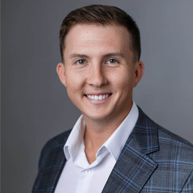 Professional headshot of Nick Robinett, smiling, in a white shirt and navy plaid blazer